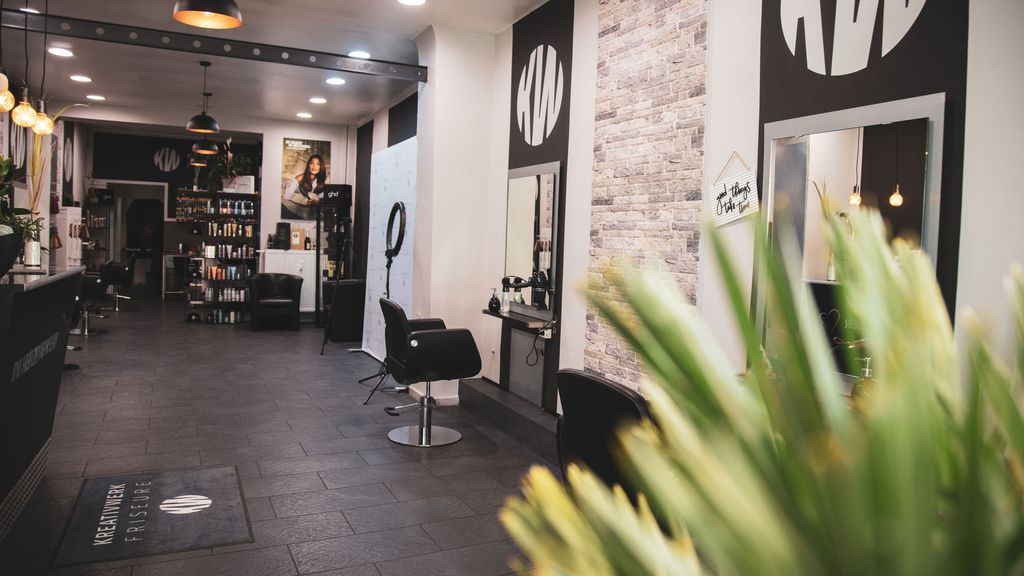 Blick in den Salon von KREATIVWERK FRISEURE mit Bedienplätzen, KW-Logo an der Wand und Produktregal